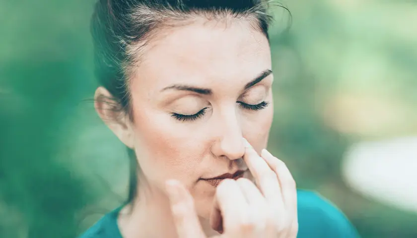Donna con occhi chiusi esegue esercizi di respirazione, toccandosi il naso con le dita.