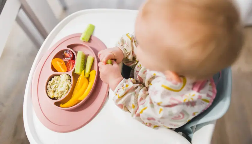 Dziecko odkrywa smaki warzyw, stosując metodę blw. Na talerzyku: pomidorki, ogórek, papryka i pasta.