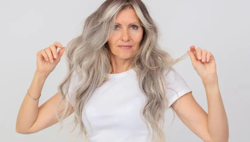 Mujer con cabello largo y ondulado, con mechas grises y rubias. Muestra cómo matizar el pelo en casa para un look radiante.