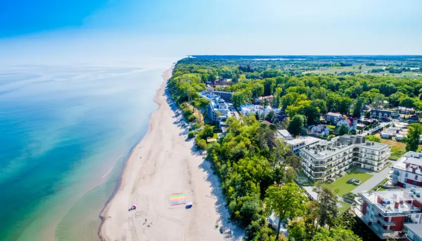 Idealny pobyt nad morzem: piaszczysta plaża, turkusowa woda i nowoczesne apartamenty wśród zieleni.