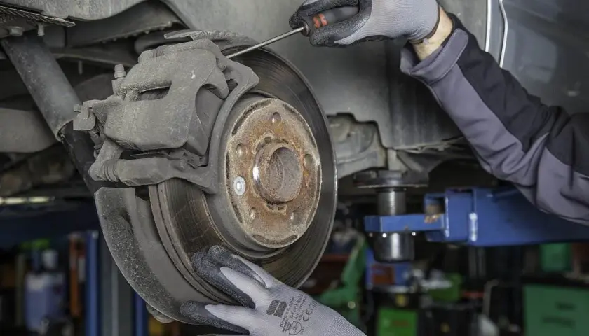 Mechanik w rękawiczkach sprawdza hamulce, by uniknąć bicia kierownicy przy hamowaniu.