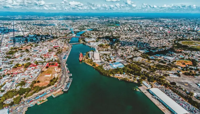 Luftaufnahme der Stadt mit einem Fluss, der sich durch sie schlängelt. Hier ist, wo Santo Domingo liegt, mit Schiffen im Hafen und vielen Gebäuden.
