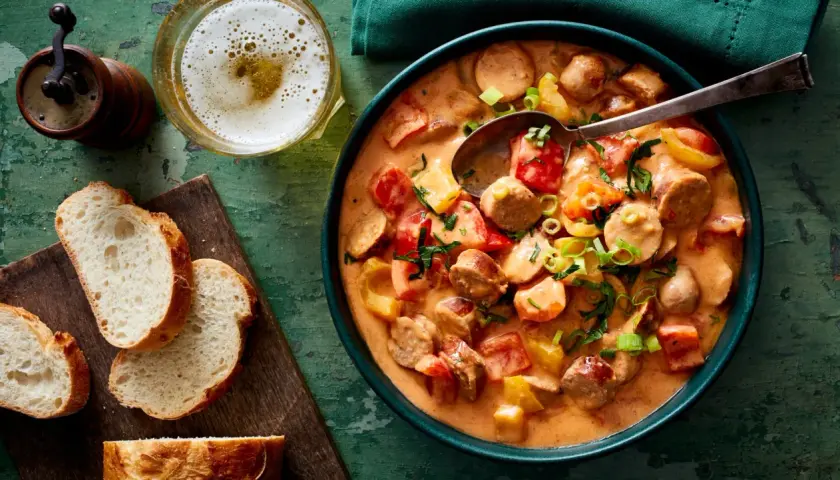 Herzhaftes Wurstgulasch mit Paprika und Tomaten, serviert mit frischem Brot und einem kühlen Bier. Ein tolles Rezept für gemütliche Abende.