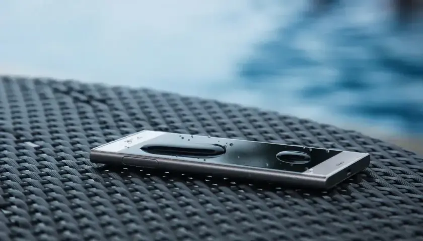 Telefon z kroplami wody na ekranie, leżący na plecionej powierzchni obok basenu. To dowód, że ip68 co oznacza – pełną ochronę przed wodą.