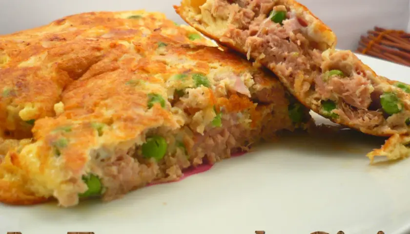 Une omelette au thon généreuse, garnie de petits pois, coupée en deux pour révéler sa texture moelleuse. Un délice simple et savoureux.