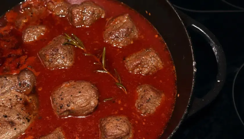 Stracotto di manzo schmort in einer tiefroten Sauce mit Rosmarin. Zarte Fleischstücke, perfekt für ein herzhaftes Gericht.