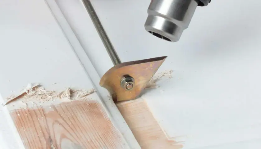 Strumento per rimuovere pittura secca dal legno, con lama affilata che solleva schegge di vernice.