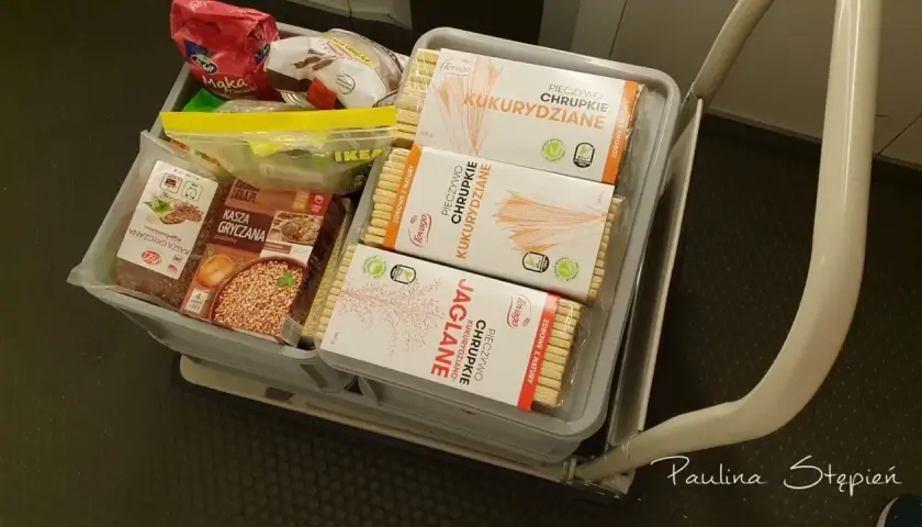 Koszyk z produktami długoterminowymi: kasza gryczana, chrupki kukurydziane i jaglane.