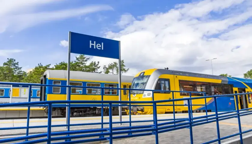 Pociąg z Władysławowa do Helu stoi na stacji. Żółto-niebieskie wagony czekają na pasażerów.