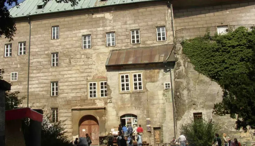 Kamienny zamek Houska z zielonym dachem i licznymi oknami, otoczony zielenią.