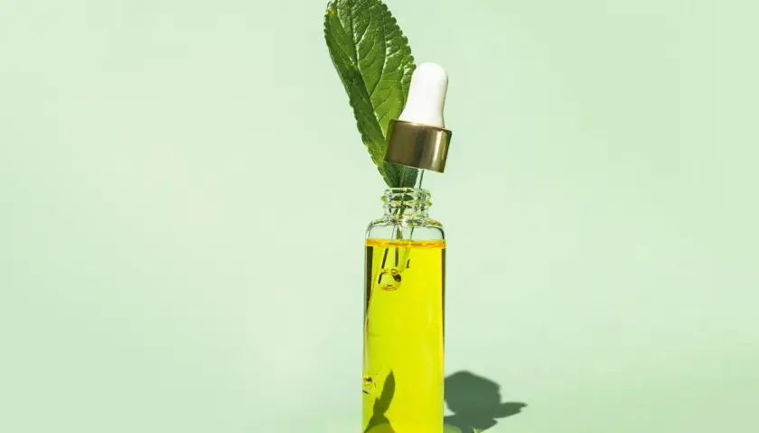En droppe av ren tee tree oil i en glasflaska med en grön blomma.