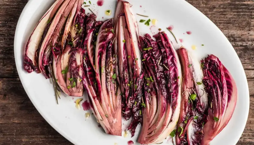 Radicchio al forno, tagliato a spicchi e condito con erbe aromatiche, servito su un piatto bianco.