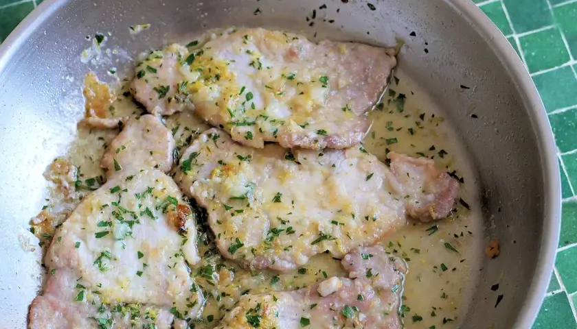 Zarte Scaloppine al Limone in einer Pfanne, garniert mit frischer Petersilie und Zitronenschale. Ein Klassiker der italienischen Küche.