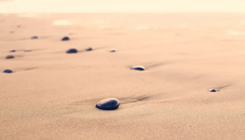 Kamienie na piaszczystej, dzikiej plaży, jak przebój Stana Borysa, tworzą ślady na piasku.