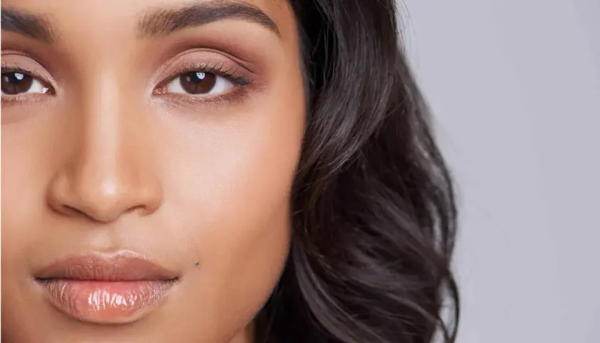 Un grain de beauté discret, comme un petit tatouage naturel, orne la joue d'une jeune femme aux yeux expressifs et aux lèvres brillantes.