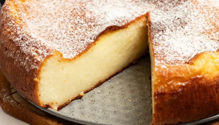 Puszysty sernik z ricotty i mascarpone, oprószony cukrem pudrem, z widocznym kawałkiem ciasta.