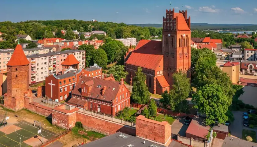 Zamek krzyżacki w Lęborku, z charakterystyczną wieżą i ceglaną architekturą, otoczony zielenią i miejską zabudową.