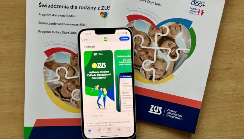 Aplikacja mZUS na telefonie pokazuje świadczenie wychowawcze 800+ dla rodziny. Ulotki ZUS informują o programach dla rodziców.