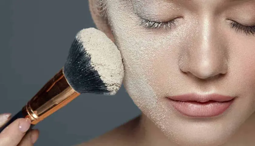 Applicazione di cipria per il baking trucco su un viso femminile. Un pennello grande raccoglie la polvere per un finish impeccabile.