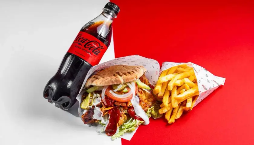 Duży kebab z frytkami i butelką Coca-Coli Zero na czerwono-białym tle.