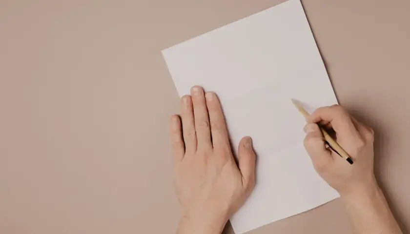 Ręce piszą list motywacyjny po angielsku na białej kartce.