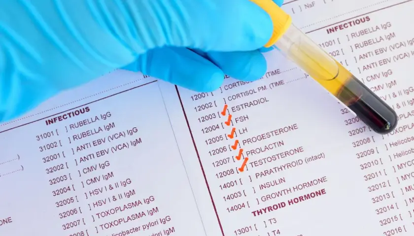 Rękawiczka pobiera próbkę krwi do badań, na liście zaznaczono estradiol.
