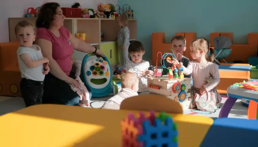 Jedna opiekunka w żłobku dogląda kilkorga dzieci bawiących się zabawkami.