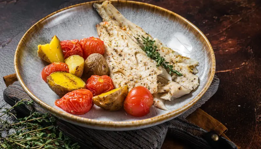 Delicioso abadejo a la plancha servido con patatas asadas y tomates cherry.