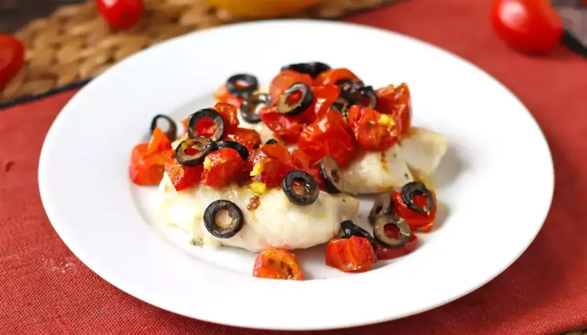 Delizioso merluzzo in friggitrice ad aria, condito con pomodorini e olive nere, pronto per essere gustato.