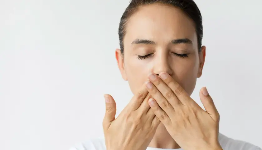 Donna con occhi chiusi copre la bocca con le mani, un'espressione di **bocca amara** sul volto.