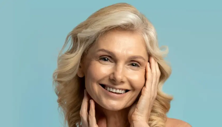Uśmiechnięta kobieta z blond włosami, której skóra lśni dzięki olejkowi kameliowemu.
