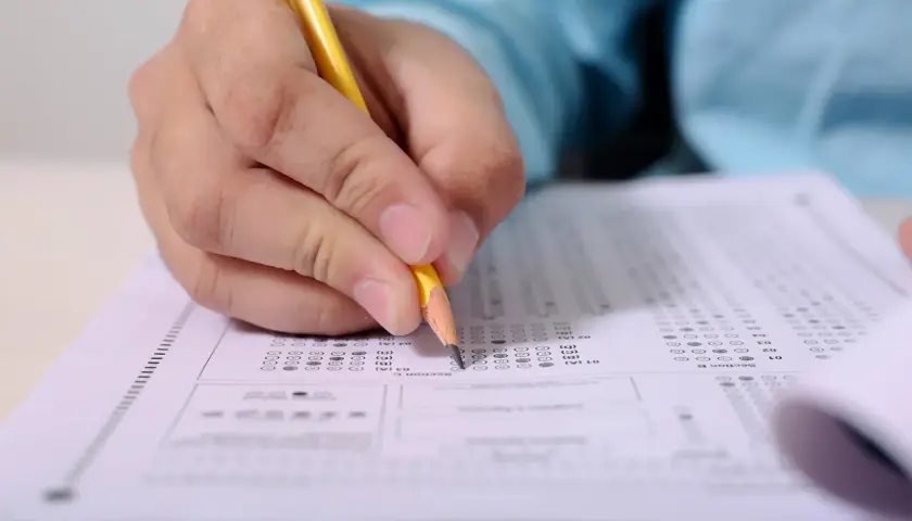 Dłoń z ołówkiem zaznacza odpowiedzi na arkuszu testowym. Przygotowanie do kursu CKZ.