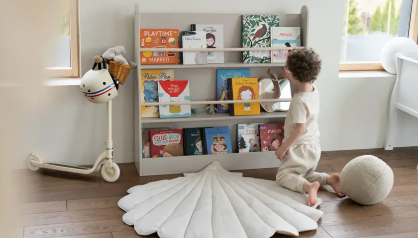 Chłopiec wybiera książkę z regału, tworząc przytulną przestrzeń do nauki i zabawy. Idealne miejsce na montessori w domu.