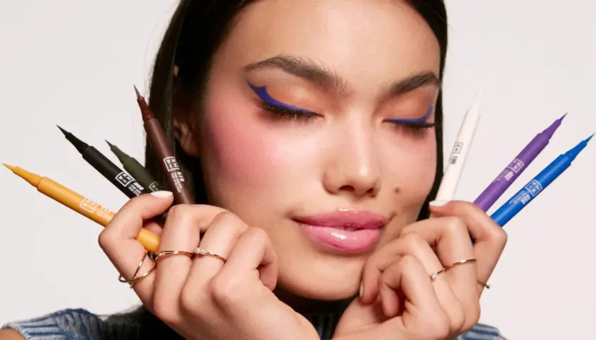 Mujer con delineado azul vibrante y varios eyeliners de colores en sus manos. Descubre qué es el eyeliner perfecto para ti.