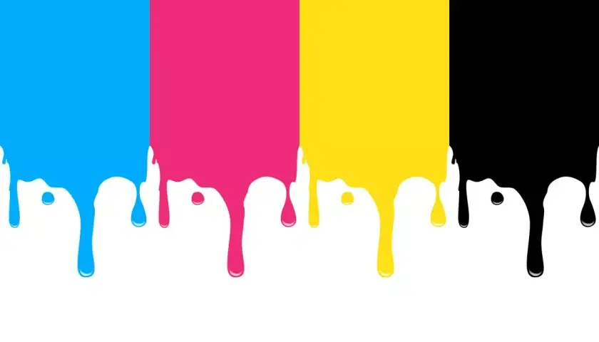 Krople farby CMYK (cyjan, magenta, żółty, czarny) spływające z góry na białe tło.