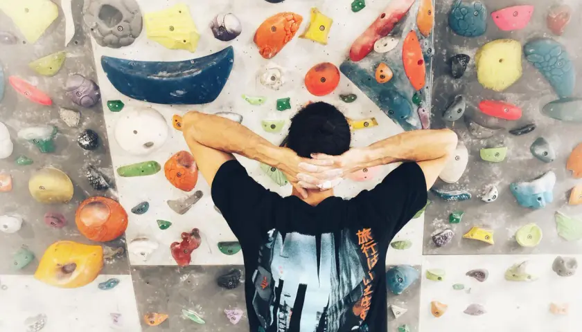 Wspinaczka bouldering na kolorowej ściance. Mężczyzna z rękami za głową, przygotowuje się do pokonania trudnej trasy.