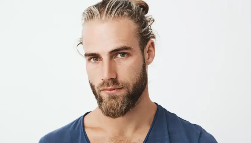Hombre con barba y moño, luciendo unas modernas mechas rubias que resaltan su estilo.