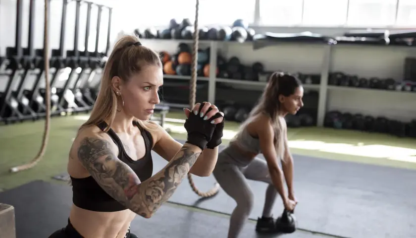 Dwie kobiety wykonują przysiady z kettlebellami. To przykład treningu funkcjonalnego, który przygotowuje ciało do codziennych czynności.