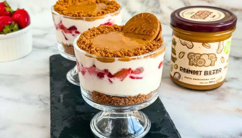 Deser z warstwami pokruszonych ciastek **Lotus**, kremu i truskawek, zwieńczony ciastkiem i masłem orzechowym.