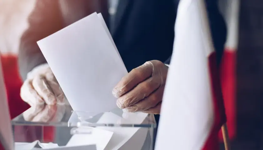 Ręka w rękawiczce wrzuca kartę do urny. Wybory, metoda Donty.