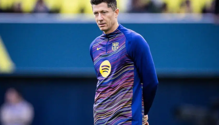 Robert Lewandowski w stroju FC Barcelona, w tle niebieska ściana. Wokół niego krążą barcelona pogłoski transferowe.