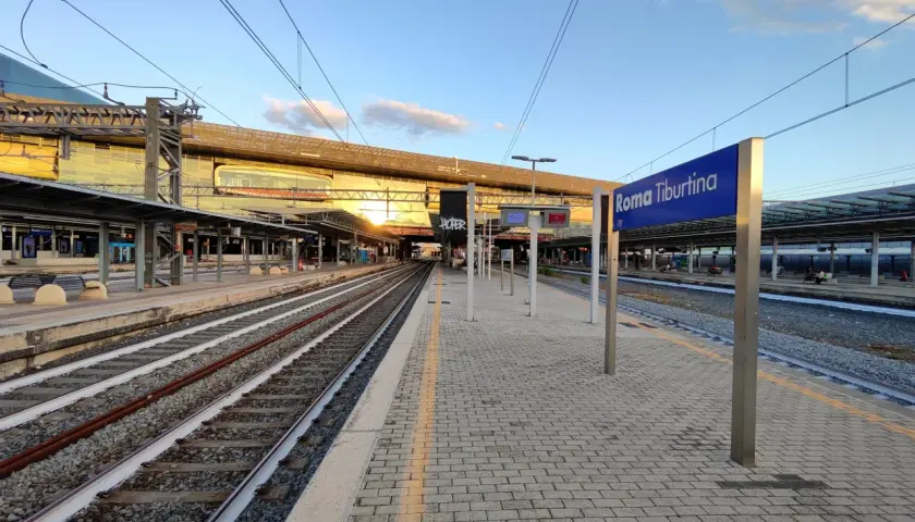 Binari e pensiline alla stazione Roma Tiburtina, con il sole che illumina la moderna architettura.