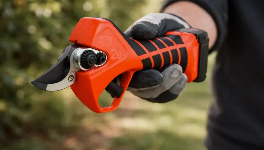 Eine Hand mit Handschuh hält eine leuchtend orangefarbene Rebschere.