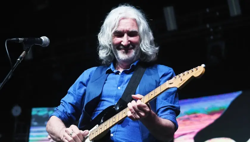 Muzyk z siwymi włosami gra na gitarze, przypominając legendarne utwory Dire Straits.