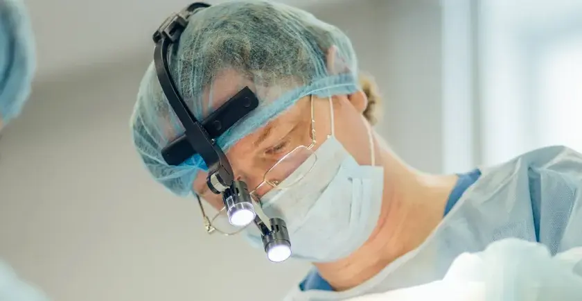 Kirurg med lupp och mask utför buccal fat removal i Sverige.