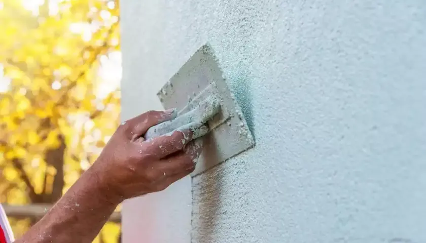 Ręka fachowca wygładza świeży tynk gąbką. Gąbkowanie tynku po jakim czasie daje najlepszy efekt?