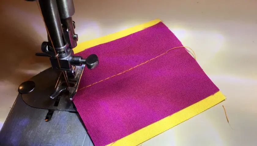 Close-up of a sewing machine needle and foot over purple fabric with a yellow border, demonstrating how to thread a sewing machine.