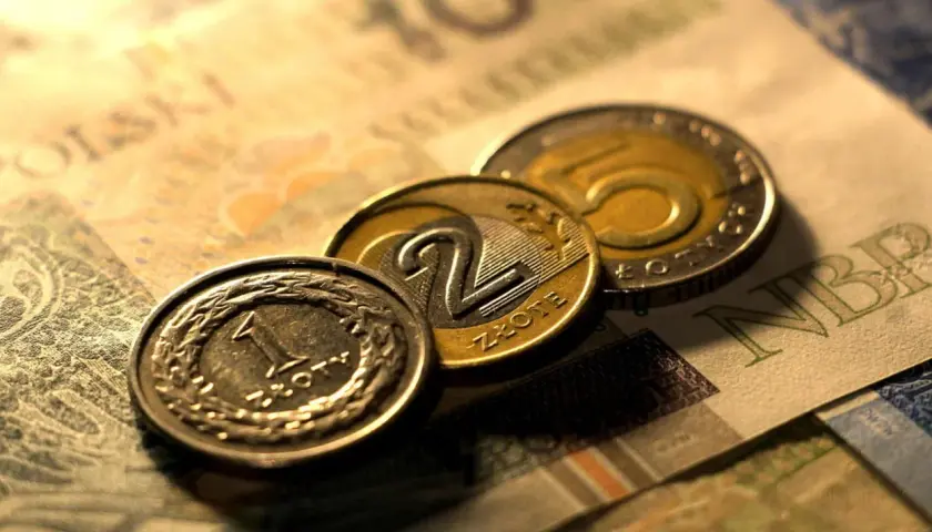 Monety 1, 2 i 5 złotych na tle banknotu 100 zł. Zastanawiasz się, przedterminowy wykup obligacji ile trwa?