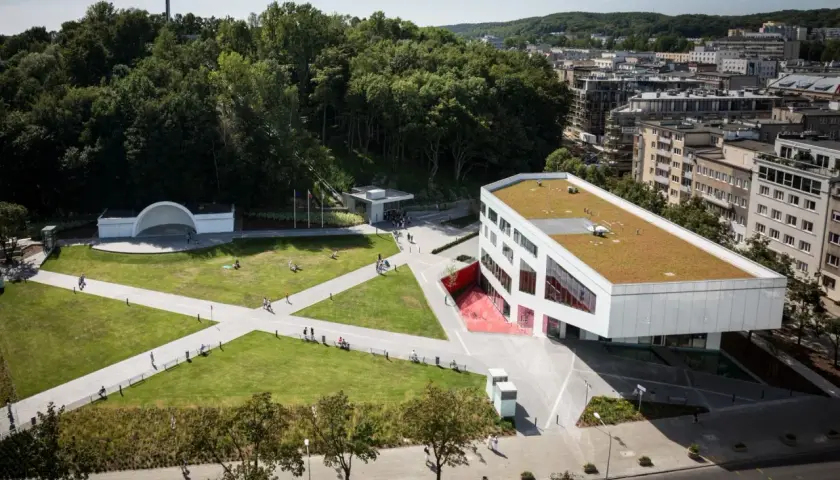 Nowoczesny budynek Gdyńskiego Centrum Filmowego z zielonym dachem, otoczony parkiem z amfiteatrem i krzyżem na wzgórzu.
