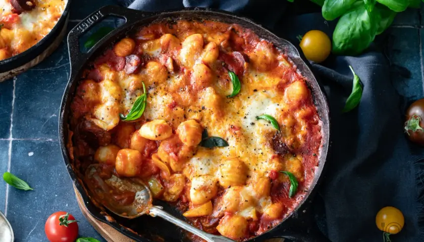 Gnocchi z pomidorami i mozzarellą zapieczone w żeliwnej patelni, ozdobione bazylią. Pyszne danie, które zachwyci każdego.